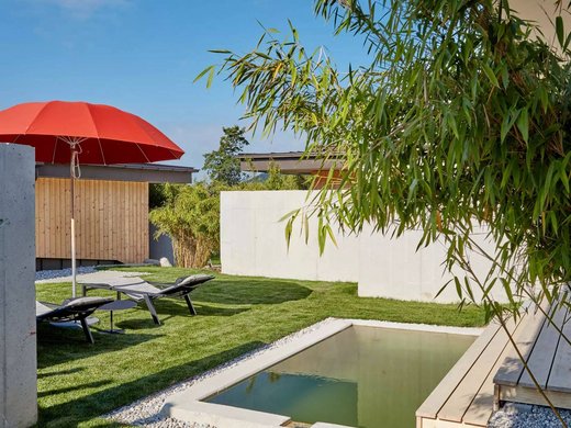 Hotel mit Whirlpool im Zimmer in Bayern Garten mit Liegestühlen, rotem Sonnenschirm und kleinem Teich