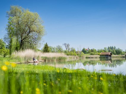 Sehenswert: Bad Tölz Grüner Fluss mit zwei Personen am Ufer und blühender Wiese im Vordergrund