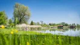 Your active summer holiday in Bavaria Green river with two people sitting on shore and blooming meadow in foreground