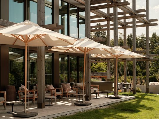 BERGEBLICK: Ihr Hotel in Bad Tölz Terrasse mit Sonnenschirmen, Sitzmöbeln und Holzstruktur vor Glasfassade
