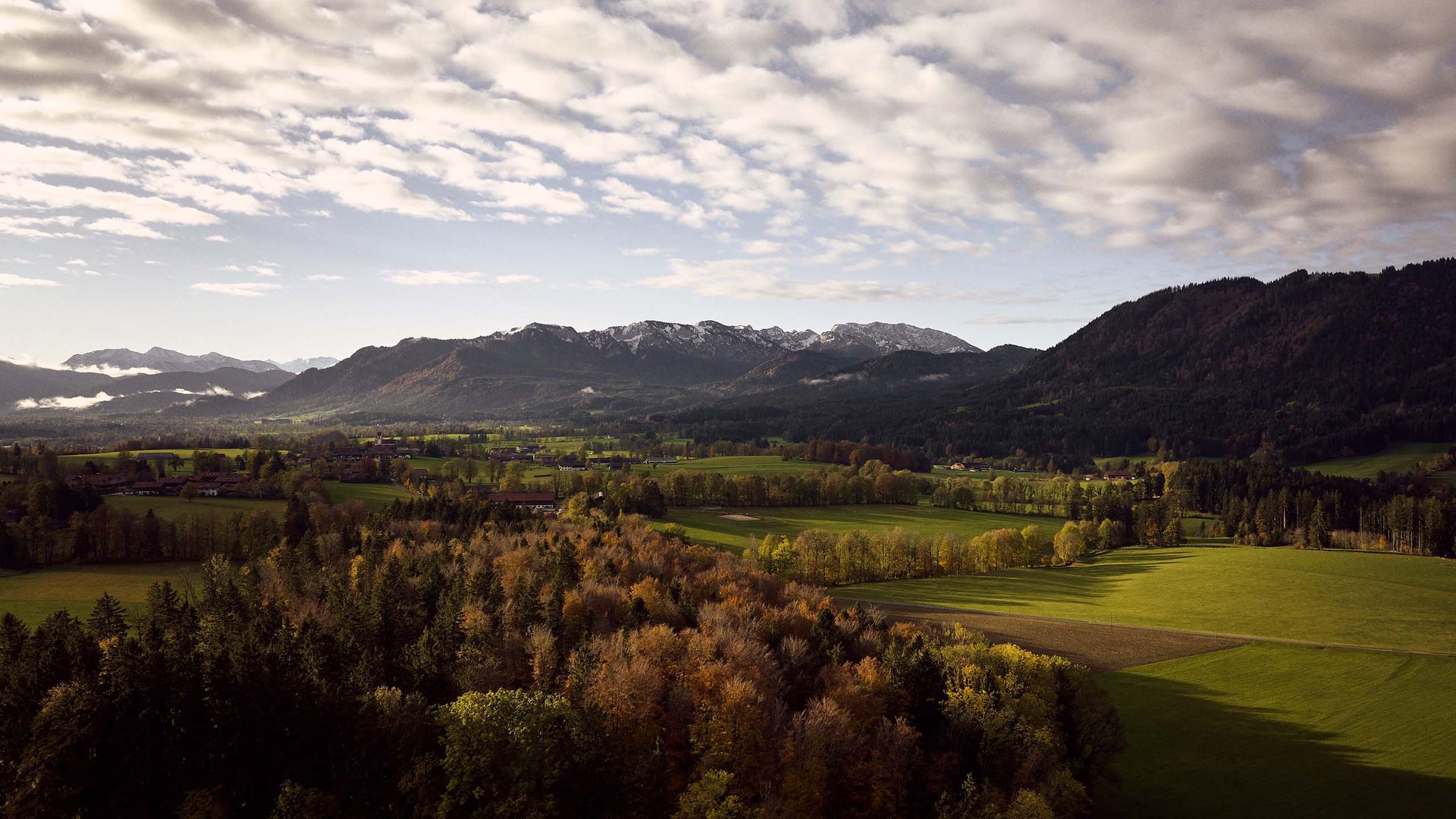 Sehenswert: Bad Tölz Herbstliche Landschaft mit farbigen Bäumen, grünen Feldern und Bergen im Hintergrund