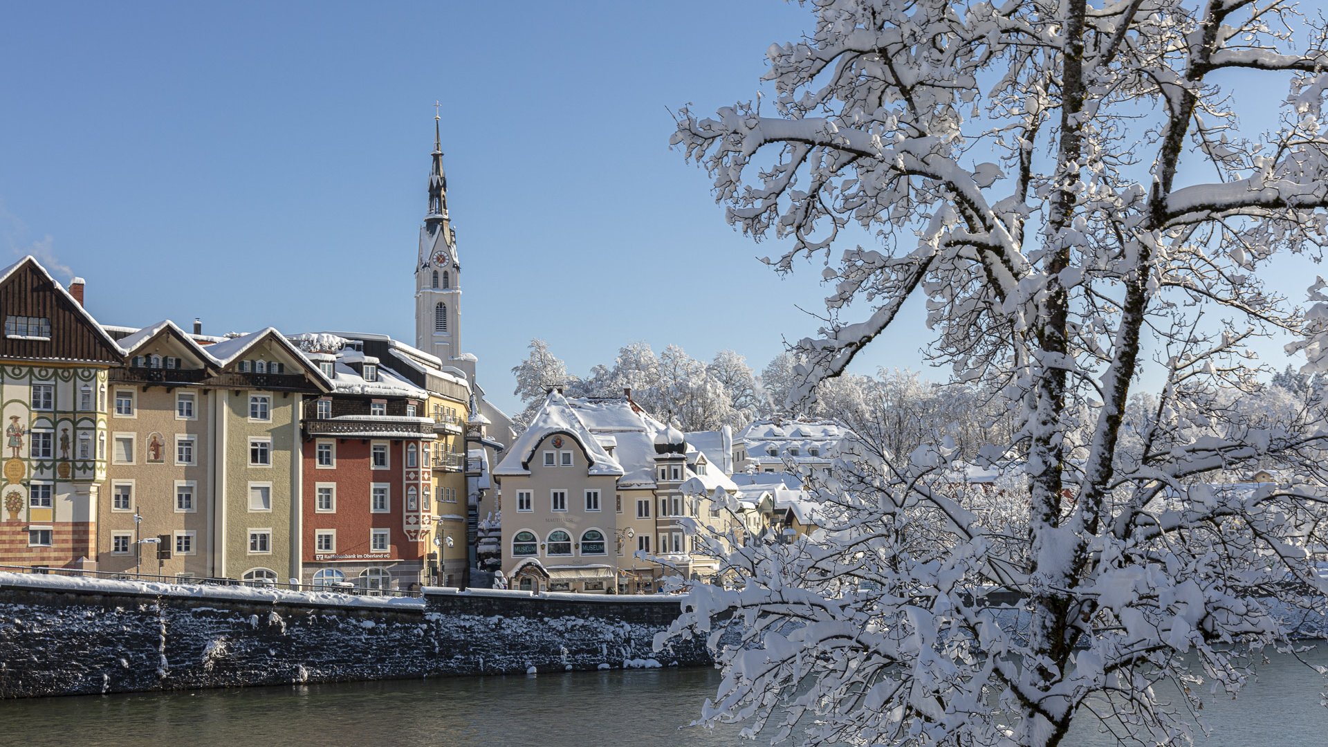 Sehenswert: Bad Tölz Winterliche Stadt mit Schnee bedeckten Häusern und Bäumen am Fluss