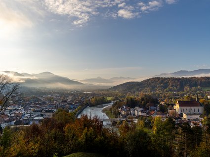 Sehenswert: Bad Tölz Blick auf eine Stadt mit Fluss, Bergen und Herbstbäumen im Morgenlicht