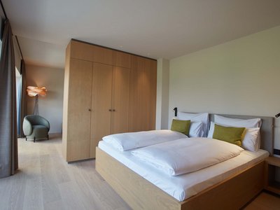 Your romantic hotel in Germany with mountain views Modern bedroom with double bed, wooden wardrobe, armchair, and floor lamp