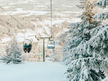 BERGEBLICK: dein Wanderhotel in Bayern Zwei Personen auf einem Sessellift über verschneitem Winterwald