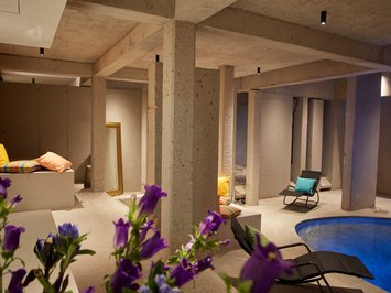 Bad Tölz: wellness & beauty Modern spa with concrete pillars, pool, lounge chairs, and colorful cushions