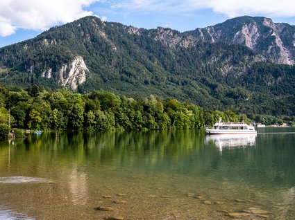 Sehenswert: Bad Tölz Fähre auf klarem See vor bewaldeten Bergen unter blauem Himmel