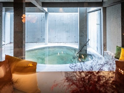 Your romantic hotel in Germany with mountain views Round indoor pool with concrete walls and colorful cushions on sofas in front