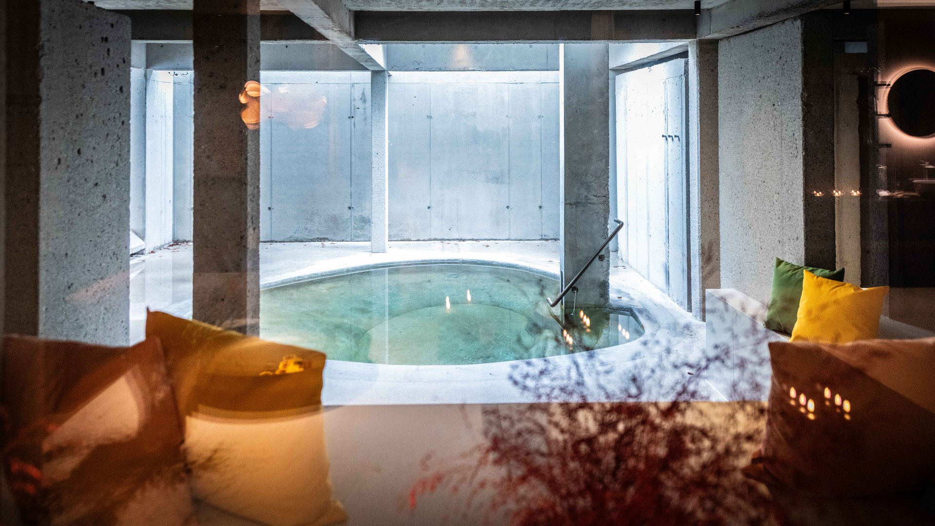 Bad Tölz: wellness & beauty Round indoor pool with concrete walls and colorful cushions on sofas in front