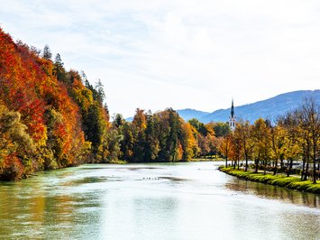 Urlaub im Aktivhotel in Bayern Herbstlicher Fluss mit bunten Bäumen und Kirchturm im Hintergrund
