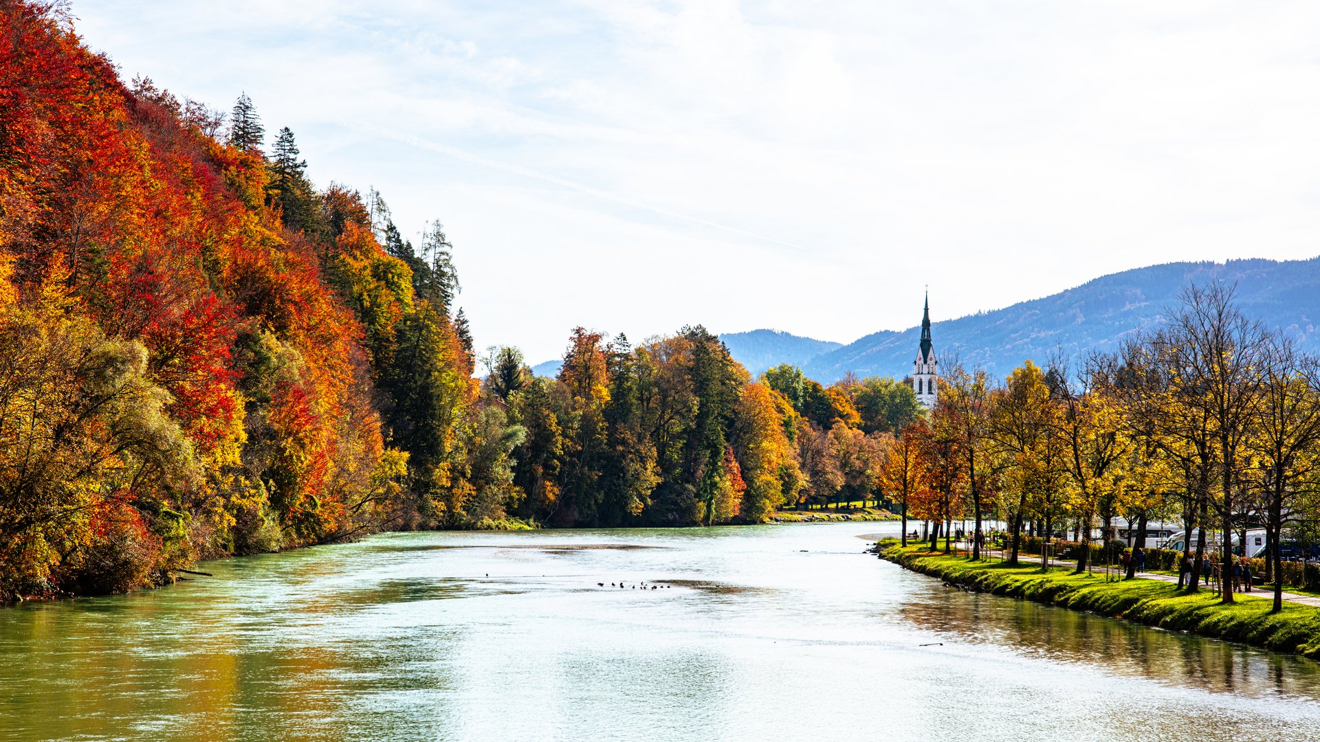 Sehenswert: Bad Tölz Herbstlicher Fluss mit bunten Bäumen und Kirchturm im Hintergrund