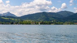 Your active summer holiday in Bavaria Sailboat on a lake with forested mountains and village under blue sky