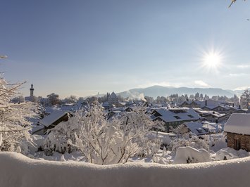Urlaub im Aktivhotel in Bayern Verschneite Stadt bei Sonnenlicht mit Bergen im Hintergrund