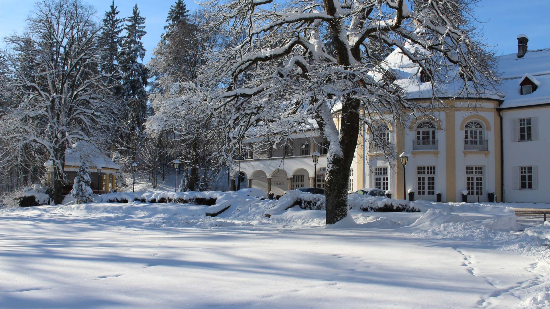 Sehenswert: Bad Tölz Schneebedecktes Anwesen mit Bäumen und großen Gebäuden an einem sonnigen Wintertag