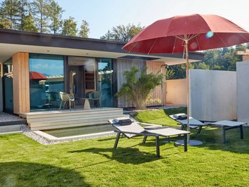 Hotel mit Whirlpool im Zimmer in Bayern Moderner Garten mit Liegestühlen, rotem Sonnenschirm und Holzterrasse