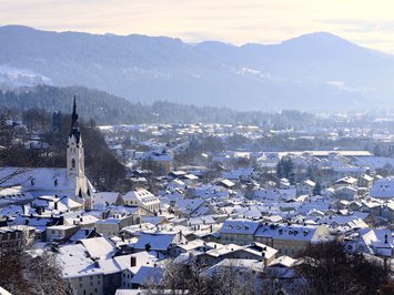 BERGEBLICK: dein Wanderhotel in Bayern Verschneite Stadt mit Kirche vor bewaldeten Bergen im Winter