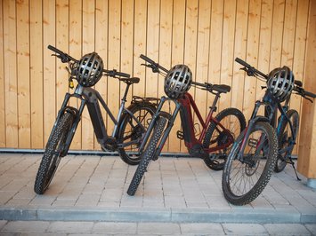 Dein Sporthotel in Bayern – Aktivurlaub im BERGEBLICK Drei E-Mountainbikes mit Helmen vor Holzwand geparkt