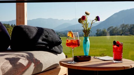 Aussicht auf Traumurlaub in Bad Tölz Getränke und Blumen auf Holztisch mit Bergblick im Hintergrund