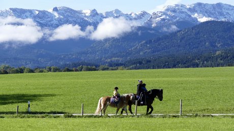 Pictures of a dream holiday in Bad Tölz People riding horses on a path with green fields and snowy mountains in the background