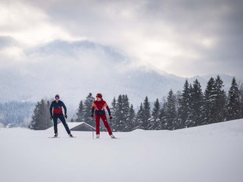 Urlaub im Aktivhotel in Bayern Zwei Skifahrer in roter und blauer Kleidung auf schneebedecktem Feld mit Bäumen und Bergen