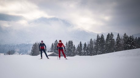 Pictures of a dream holiday in Bad Tölz Two skiers in red and blue outfits on snow-covered field with trees and mountains