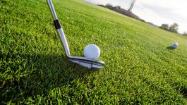 Urlaub in der Natur Bayerns Golfball liegt auf Gras neben einem Golfschläger vor hellem Himmel
