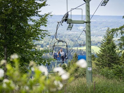 BERGEBLICK: dein Wanderhotel in Bayern Mutter und Kind auf Sessellift im grünen Wald mit Bergpanorama