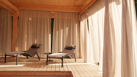 Aussicht auf Traumurlaub in Bad Tölz Zwei Liegestühle auf Holzterrasse mit Vorhängen im warmen Sonnenschein