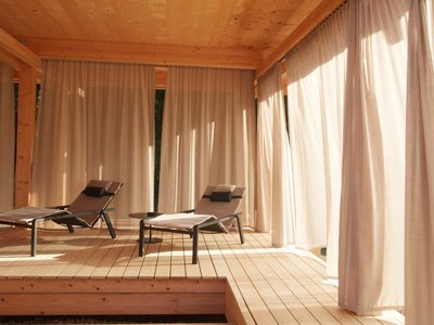 Dein Aktivurlaub im Hotel mit Fitnessstudio in Bayern Zwei Liegestühle auf Holzterrasse mit Vorhängen im warmen Sonnenschein