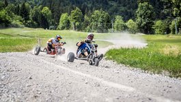 Urlaub in der Natur Bayerns Zwei Menschen fahren auf Dreirädern auf einem Schotterweg in grüner Landschaft