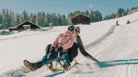Pictures of a dream holiday in Bad Tölz Couple sledding together on a snowy slope with cabins in the background