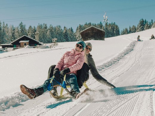 Your active holiday in Bavaria in Bad Tölz Couple sledding together on a snowy slope with cabins in the background