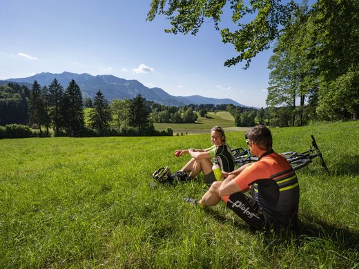 Your active holiday in Bavaria in Bad Tölz Two cyclists resting on a meadow with mountain view in the background