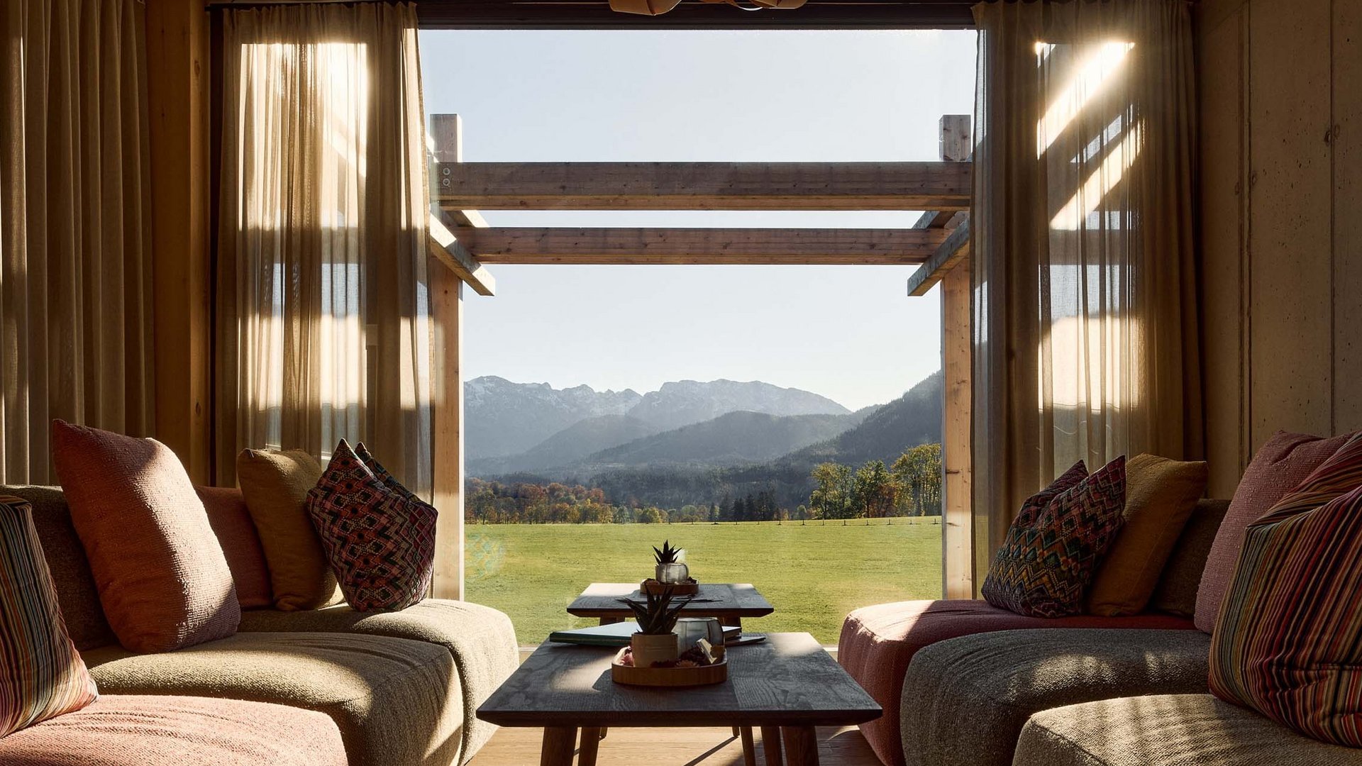 Warum ins BERGEBLICK? Gemütliches Wohnzimmer mit Blick auf grüne Wiese und Berge durch großes Fenster