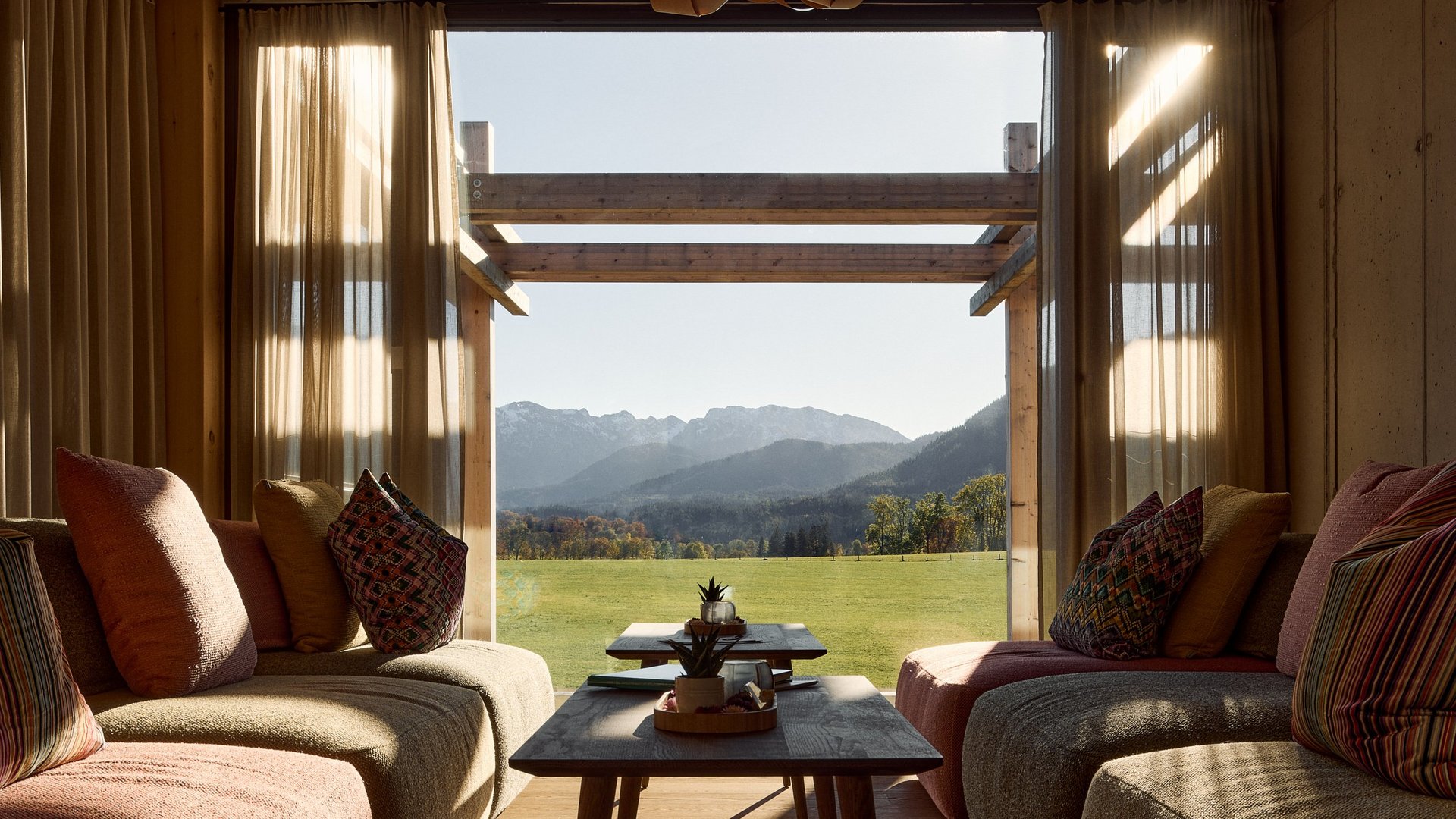 Warum ins BERGEBLICK? Gemütliches Wohnzimmer mit Blick auf grüne Wiese und Berge durch großes Fenster