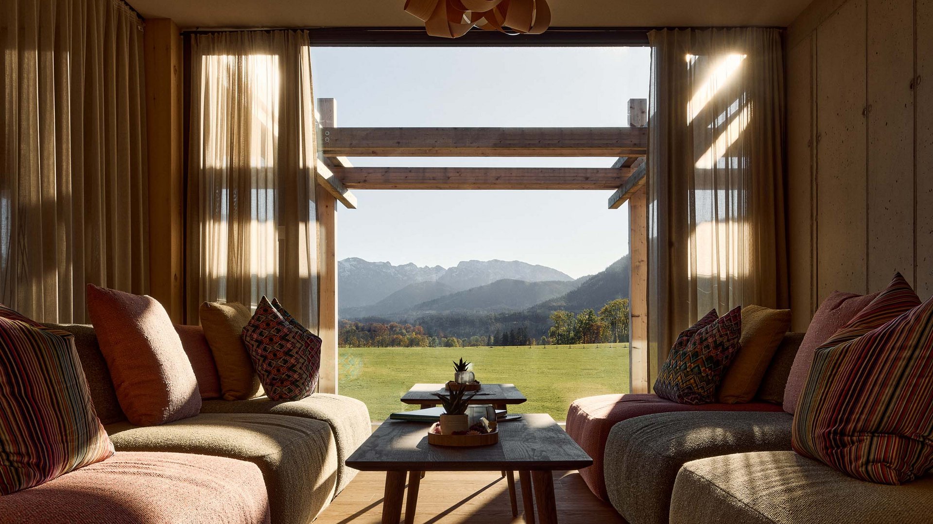 Hotel BERGEBLICK für Wellness in Bad Tölz Gemütliches Wohnzimmer mit Blick auf grüne Wiese und Berge durch großes Fenster