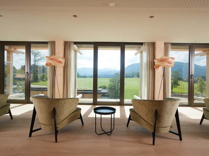 Dein Natururlaub in Bayern: BERGEBLICK Moderne Stühle und Lampe mit Blick auf grünes Feld und Berge durch große Fenster