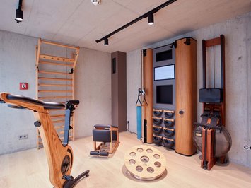 Dein Sporthotel in Bayern – Aktivurlaub im BERGEBLICK Moderner Heimtrainer mit Holz und Fitnessgeräte in einem Raum mit Betondecken