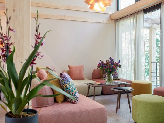 Wissenswertes aus Bad Tölz Gemütliches Wohnzimmer mit bunten Sofas, Blumen und großen Fenstern