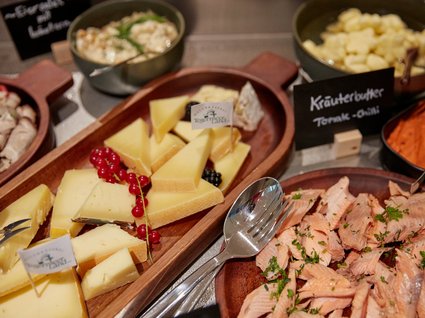 Bad Tölz: Hotel mit regionalem Frühstück Verschiedene Käsesorten und geräucherter Fisch auf Holzplatten mit Kräuterbutter