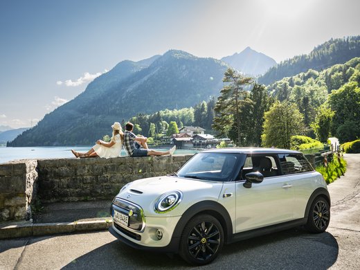 Your active holiday in Bavaria in Bad Tölz Couple sitting on wall overlooking lake and mountains, white Mini Cooper parked nearby
