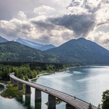 BERGEBLICK: Ihr Hotel in Bad Tölz Brücke über einen See mit Bergen und bewölktem Himmel im Hintergrund