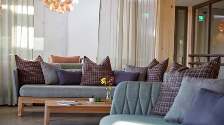 Aussicht auf Traumurlaub in Bad Tölz Modernes Wohnzimmer mit grauen Sofas, gemusterten Kissen und Holztisch mit Blumen