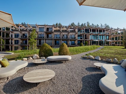 Dein Natururlaub in Bayern: BERGEBLICK Moderner Hotelgarten mit geschwungenen Sofas und Blick auf Holzbau mit Balkon
