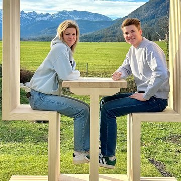 Holiday at BERGEBLICK in Bad Tölz Two people sitting at a wooden table with mountains and blue sky in the background