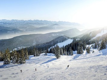 Winterurlaub in Bayern im BERGEBLICK Verschneite Berge mit Skifahrern und sonnigem Himmel