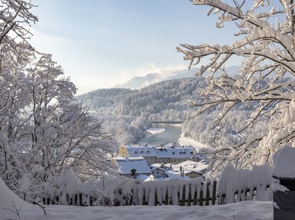 Sehenswert: Bad Tölz Schneebedeckte Bäume, Häuser und ein Fluss in einer winterlichen Berglandschaft