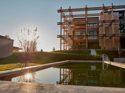 Your romantic hotel in Germany with mountain views Modern wooden architecture by a calm pool at sunset