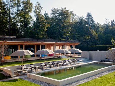 Kurzurlaub in Bayern? Im BERGEBLICK Pool mit Liegestühlen und Sonnenschirmen vor modernem Holzhaus im Garten