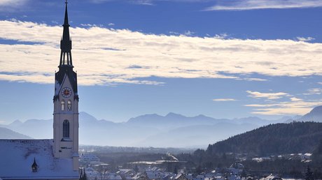 Pictures of a dream holiday in Bad Tölz Church tower over snow-covered village with mountains and blue sky in the background